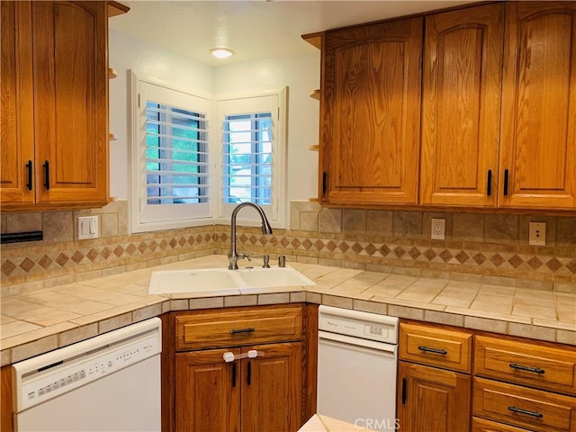 kitchen featuring tasteful backsplash, tile counters, dishwasher, brown cabinets, and a sink