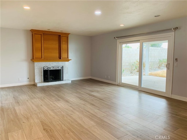 unfurnished living room featuring a fireplace with raised hearth, light wood-style floors, and baseboards