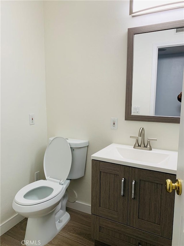 bathroom featuring toilet, vanity, baseboards, and wood finished floors