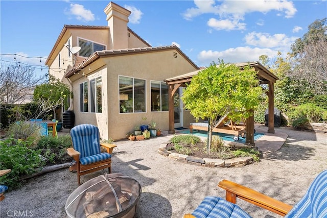 back of house featuring a tiled roof, a fire pit, a patio, and stucco siding