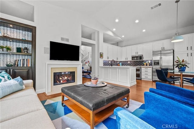 living area with light wood-type flooring, a glass covered fireplace, visible vents, and recessed lighting