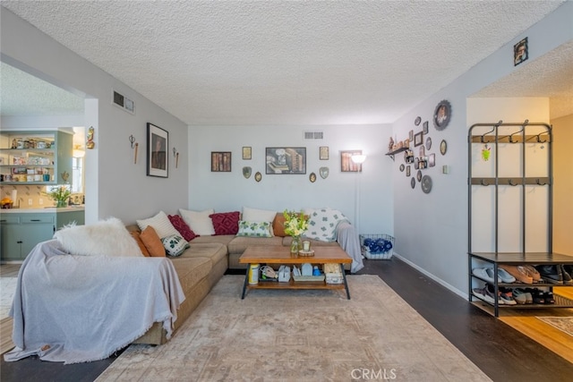 living area with baseboards, a textured ceiling, visible vents, and wood finished floors