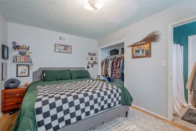 bedroom featuring a closet, visible vents, a textured ceiling, and light wood finished floors