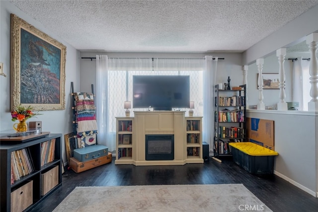 living room featuring a glass covered fireplace, dark wood-style flooring, a textured ceiling, and baseboards