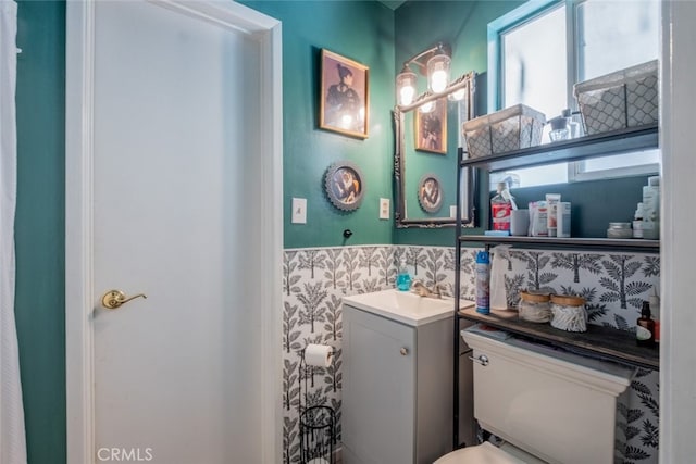 half bathroom featuring a wainscoted wall, vanity, and wallpapered walls