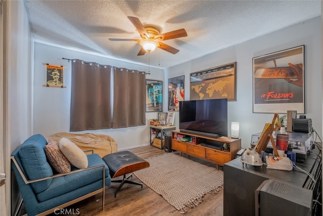 living area with ceiling fan, a textured ceiling, and wood finished floors