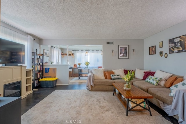 living area featuring a glass covered fireplace, visible vents, a textured ceiling, and wood finished floors