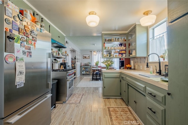 kitchen with open shelves, stainless steel appliances, light countertops, a sink, and green cabinetry