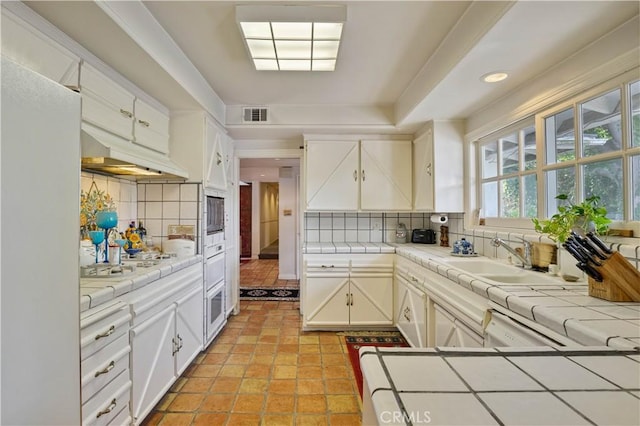 kitchen with tile counters, white cabinets, visible vents, and a sink