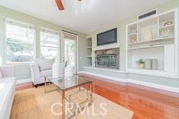 living room featuring built in shelves, a fireplace with raised hearth, visible vents, ceiling fan, and baseboards