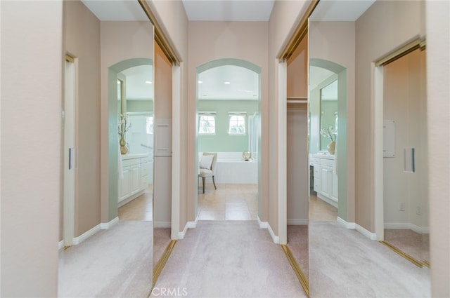 hall with baseboards, arched walkways, and light colored carpet