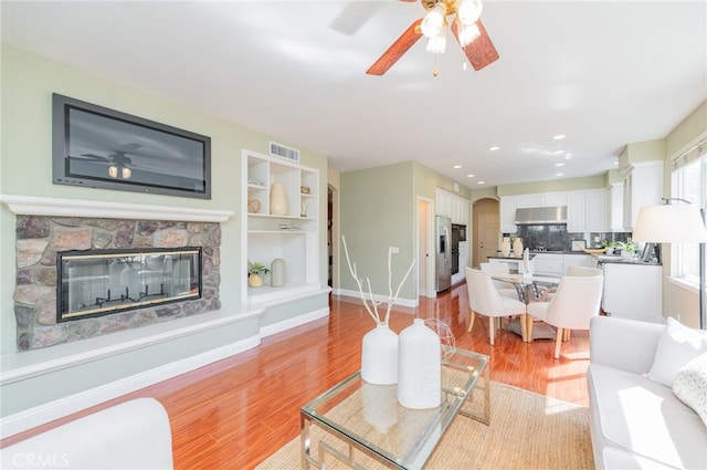 living room with light wood-style flooring, a fireplace, visible vents, and baseboards