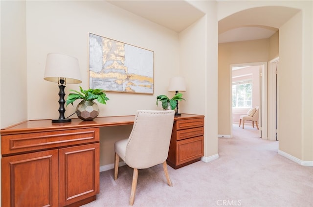 home office with arched walkways, light colored carpet, and baseboards