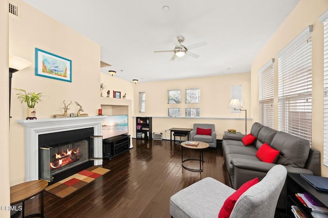 living room with dark wood-style floors, visible vents, a fireplace with flush hearth, and a ceiling fan