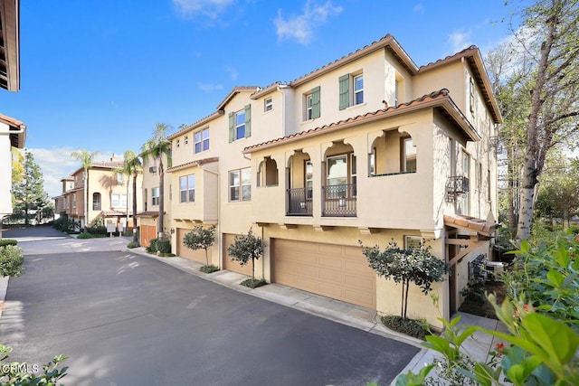 mediterranean / spanish home featuring a residential view, a tiled roof, an attached garage, and stucco siding