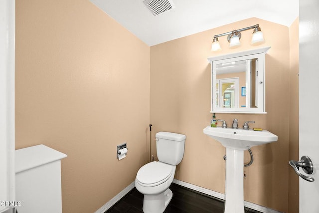 half bathroom with baseboards, visible vents, toilet, wood finished floors, and a sink