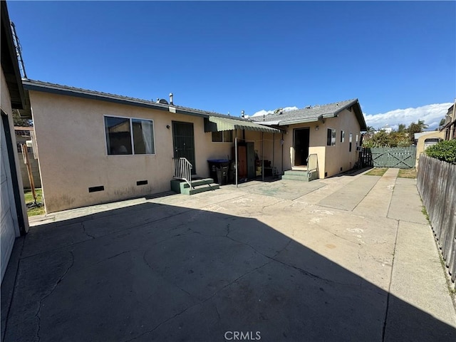 rear view of house featuring entry steps, a patio, fence, crawl space, and stucco siding