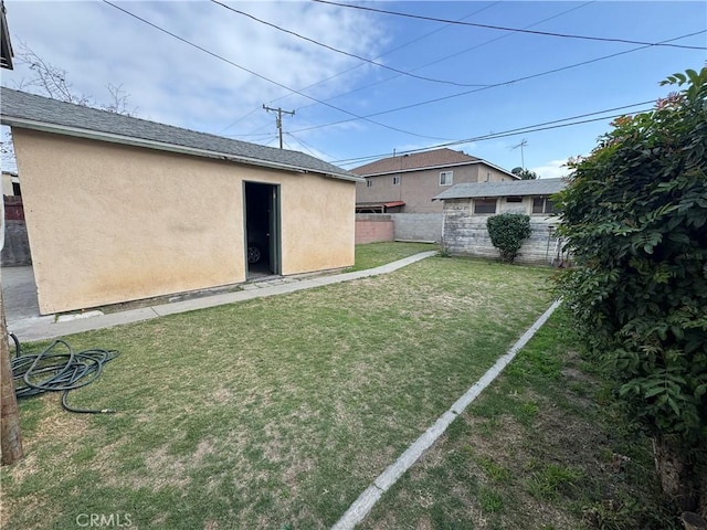 rear view of house with an outbuilding, fence, roof with shingles, a lawn, and stucco siding