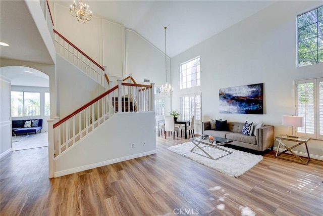 living area featuring an inviting chandelier, stairway, high vaulted ceiling, and wood finished floors