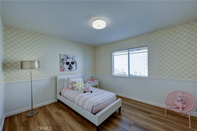 bedroom with a wainscoted wall, baseboards, wood finished floors, and wallpapered walls