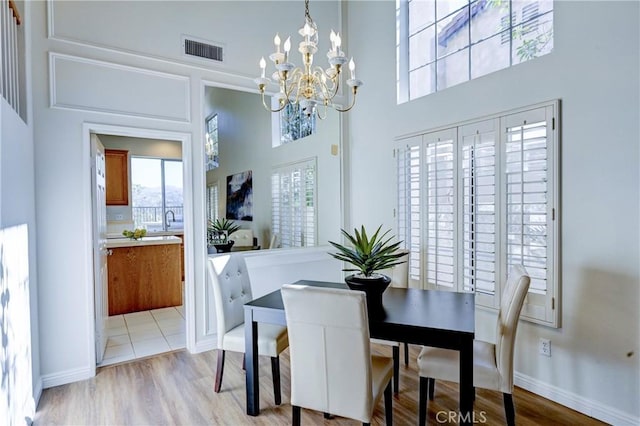 dining area with a high ceiling, visible vents, a chandelier, and wood finished floors