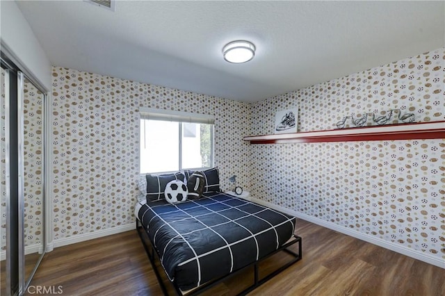 bedroom featuring a closet, wood finished floors, baseboards, and wallpapered walls