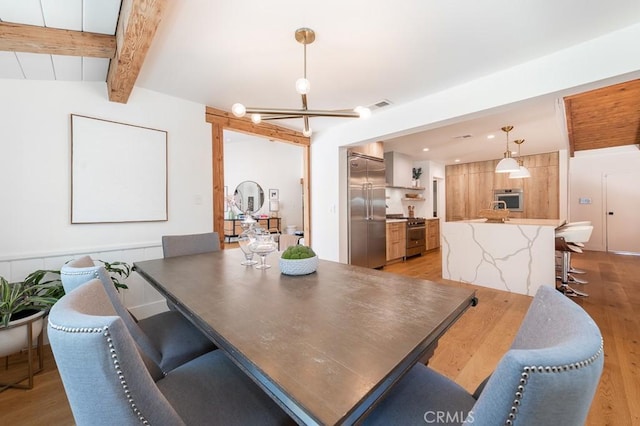 dining area with a chandelier, light wood-style flooring, visible vents, and lofted ceiling with beams