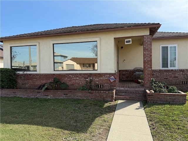 view of front of home with crawl space, brick siding, a front lawn, and stucco siding