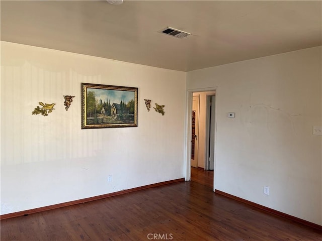 unfurnished room with dark wood-style floors, visible vents, and baseboards