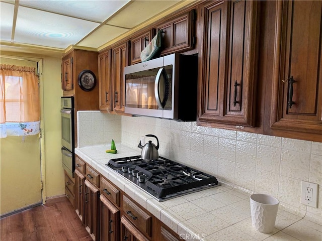 kitchen with dark wood-style flooring, a warming drawer, stainless steel appliances, tile counters, and tasteful backsplash