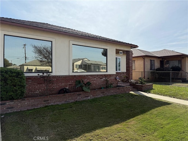 view of home's exterior featuring stucco siding, a yard, brick siding, and fence