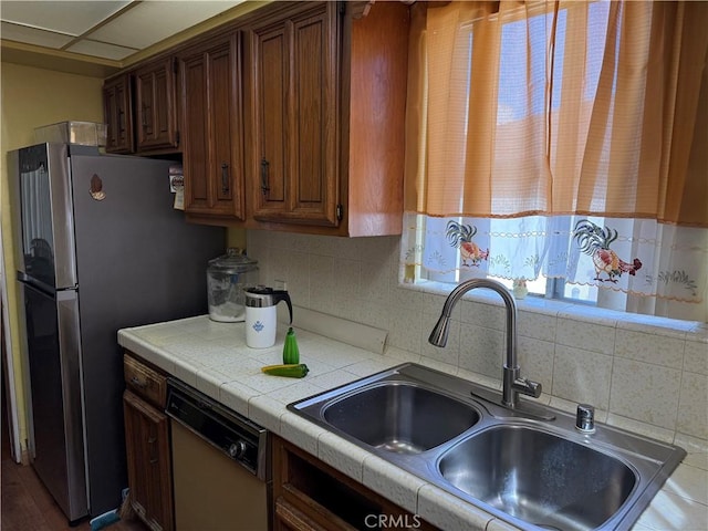 kitchen featuring tile counters, a sink, decorative backsplash, and dishwashing machine