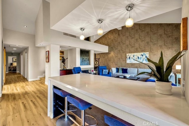 kitchen with baseboards, open floor plan, wood finished floors, decorative light fixtures, and high vaulted ceiling