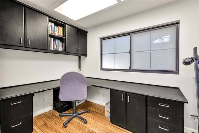 office with light wood finished floors, baseboards, and built in desk