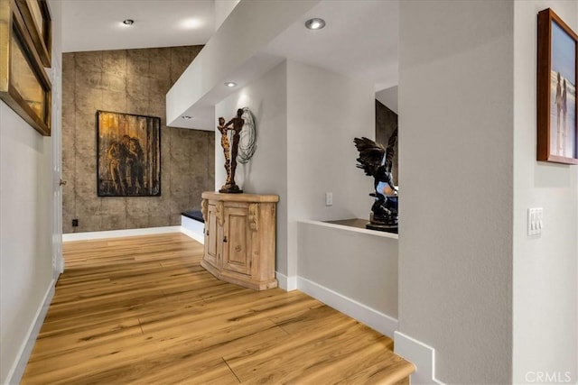 hall featuring an accent wall, recessed lighting, baseboards, and wood finished floors