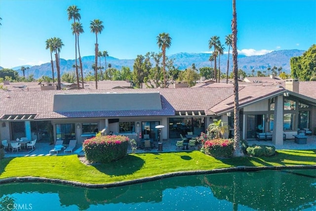 rear view of property with a patio area, a tile roof, a water and mountain view, and a yard