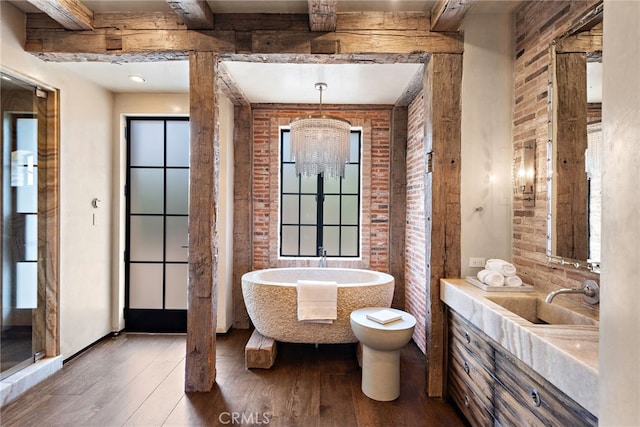 full bath with brick wall, wood-type flooring, a freestanding tub, and beam ceiling