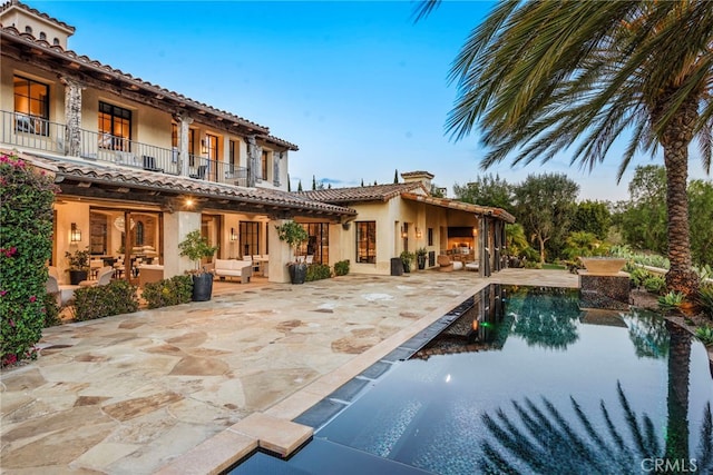 rear view of house with a patio, a balcony, an outdoor living space, an outdoor pool, and stucco siding