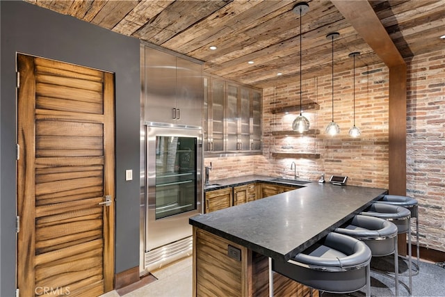 kitchen featuring dark countertops, wood ceiling, a sink, brick wall, and a peninsula