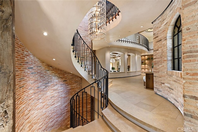 foyer featuring recessed lighting, stairway, a towering ceiling, brick wall, and a chandelier