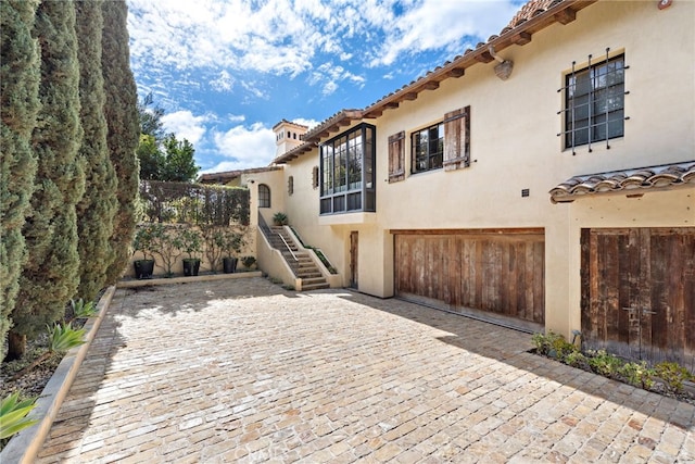 view of front facade featuring an attached garage, stairs, a tiled roof, decorative driveway, and stucco siding