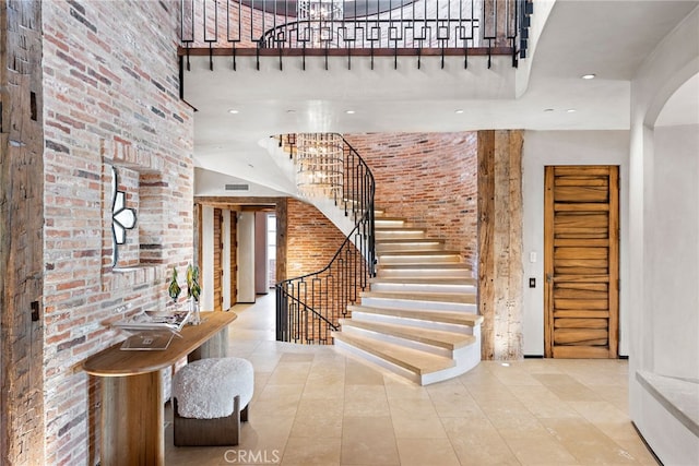 entrance foyer featuring arched walkways, brick wall, stairway, a high ceiling, and recessed lighting