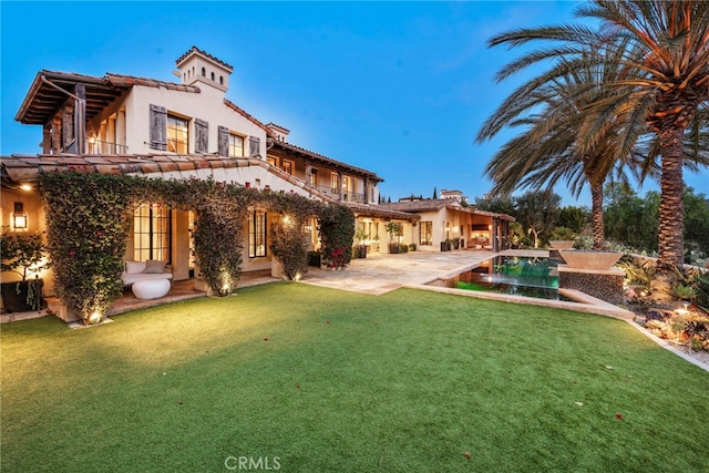 rear view of property featuring an outdoor pool, a tile roof, a yard, a patio area, and stucco siding