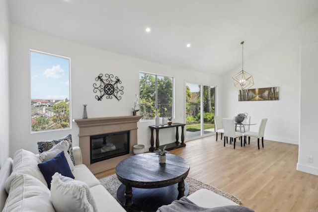 living room with a notable chandelier, baseboards, vaulted ceiling, light wood-type flooring, and a glass covered fireplace