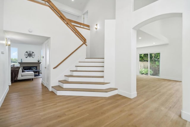 stairway featuring a towering ceiling, a fireplace, arched walkways, and wood finished floors