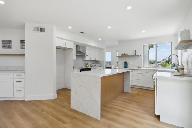 kitchen with a kitchen island, white cabinetry, light countertops, wall chimney range hood, and open shelves