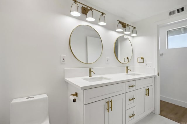 bathroom with double vanity, visible vents, toilet, and a sink