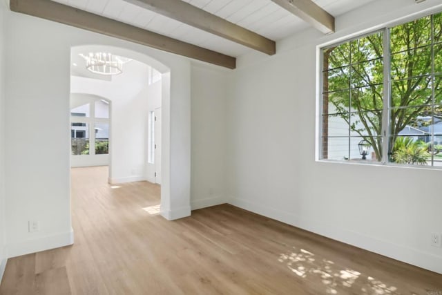 unfurnished room with arched walkways, light wood-type flooring, beam ceiling, and baseboards