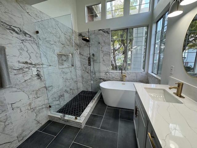 full bath featuring a freestanding bath, vanity, a marble finish shower, and tile patterned floors