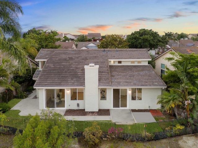 back of property at dusk featuring a chimney, a patio area, a fenced backyard, and stucco siding